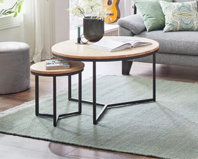 Zwei runde Couchtische mit Holzplatte und schwarzem Metallgestell auf Teppich im Wohnzimmer. Modernes Wohnaccessoire als funktionale Ergänzung zur Sofalandschaft.